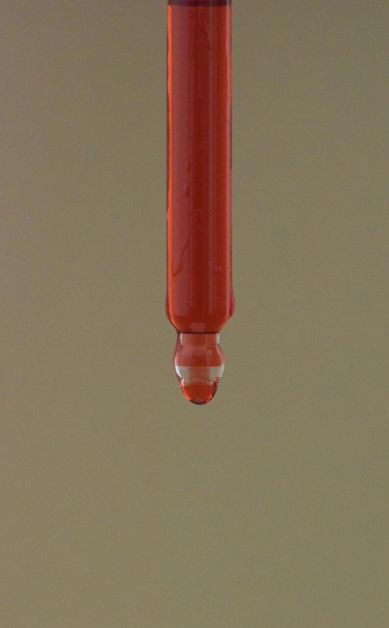 May include: A close-up of a red liquid dripping from a glass dropper.