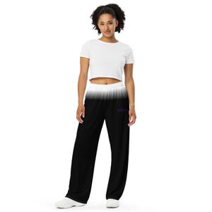 Könnte beinhalten: Schwarz-weiß-Ombre-Jogginghose mit weitem Bein. Die Hose hat einen weißen Bund, der in Schwarz übergeht. Das Wort "Unfuck" ist lila auf dem linken Bein aufgedruckt. Das Model trägt ein weißes Crop-Top.