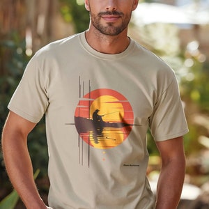 May include: A beige t-shirt with a graphic print of a person fishing at sunset. The graphic features a red, orange, and yellow sun with a silhouette of a person fishing in a boat. The text "Pure Belize" is printed below the graphic.