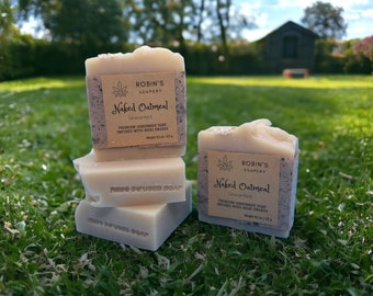 May include: Three rectangular bars of beige Naked Oatmeal soap from Robin's Soapery. Each bar features a tan paper label with black text reading Naked Oatmeal, Unscented, and Weight 4.5 oz / 127 g. The soap bars have a textured top and side.