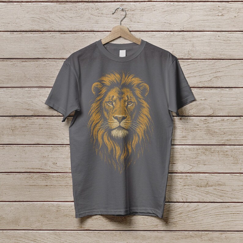 May include: A gray t-shirt featuring a detailed illustration of a lion's head. The lion's mane is a golden-brown color, and the shirt is hanging on a wooden hanger against a wood-paneled background.