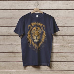 May include: Navy blue t-shirt featuring a detailed illustration of a lion's head with a golden mane. The lion's face is centered, showcasing its intense gaze and intricate fur details. The shirt is hanging on a wooden hanger against a wood-paneled background.