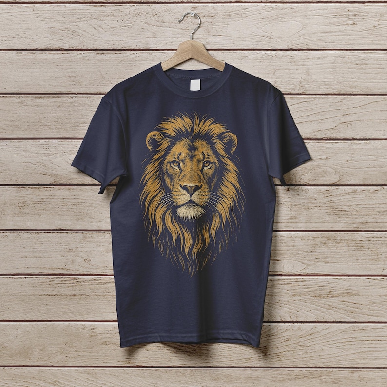 May include: Navy blue t-shirt featuring a detailed illustration of a lion's head with a golden mane. The lion's face is centered, showcasing its intense gaze and intricate fur details. The shirt is hanging on a wooden hanger against a wood-paneled background.