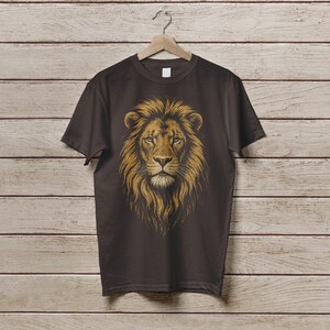 May include: A dark brown t-shirt featuring a detailed illustration of a lion's head. The lion's mane is a golden-brown color, and the face is intricately detailed. The shirt is hanging on a wooden hanger against a wooden background.