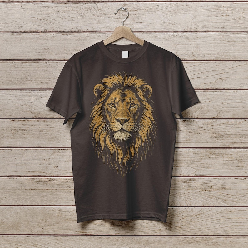 May include: A dark brown t-shirt featuring a detailed illustration of a lion's head. The lion's mane is a golden-brown color, and the face is intricately detailed. The shirt is hanging on a wooden hanger against a wooden background.
