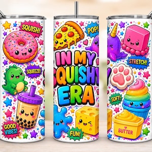 May include: A cylindrical metal tumbler with a straw featuring a colorful pattern of cartoon characters, food items, and stars. The text "IN MY SQUISHY ERA" is printed in large, bold, multi-colored letters, surrounded by words like "SQUISH!", "POP!", "STRETCH!", "SOFT!", "FUN!", and "BUTTER".