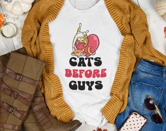 May include: White t-shirt featuring a graphic of two cats inside a pink heart. The text "Cats Before Guys" is printed below the heart.