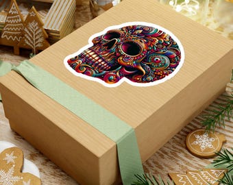 May include: A colorful skull sticker with intricate patterns in shades of red, orange, blue, and green. The sticker is placed on a brown gift box with a light green ribbon. The design is detailed and eye-catching.