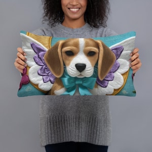 May include: A rectangular throw pillow featuring a brown and white beagle dog with large white and purple embroidered wings. The dog wears a bright turquoise bow tie around its neck. The background is a textured light blue with a golden circular frame.