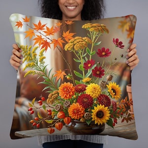 May include: A square throw pillow featuring a vibrant autumn floral arrangement. The design displays orange maple leaves, yellow goldenrod, red cosmos, orange and red dahlias, yellow sunflowers, and orange physalis berries in a dark bowl.
