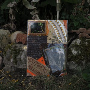 Peut inclure: Œuvre d'art en techniques mixtes de forme rectangulaire. Elle intègre diverses textures et matériaux, dont du papier, du tissu et un revêtement en plastique transparent. L'œuvre présente une petite image encadrée, du texte manuscrit et le mot "PYTHON" sur une étiquette en bois.