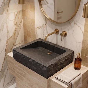 Pu&ograve; includere: Un lavabo rettangolare in pietra grigio scuro con un rubinetto in ottone e un dosatore di sapone abbinato. Il lavabo &egrave; appoggiato su un piano di lavoro in pietra colorata con un asciugamano beige piegato. Il bagno ha pareti in marmo e piastrelle.