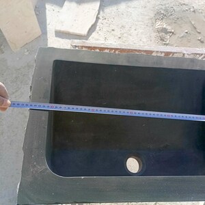 Pu&ograve; includere: Un lavandino rettangolare in pietra grigio scuro con interno arrotondato. Un metro a nastro &egrave; posto sopra il lavandino, indicando le sue dimensioni. Il lavandino ha un foro di scarico ed &egrave; inserito in una cornice di pietra grezza.