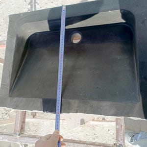 Pu&ograve; includere: Un lavandino rettangolare in pietra grigio scuro con un foro di scarico centrale. Un metro a nastro mostra la lunghezza del lavandino. Il lavandino ha una superficie leggermente strutturata e un bordo esterno rialzato. Il lavandino misura circa 76 cm di lunghezza.