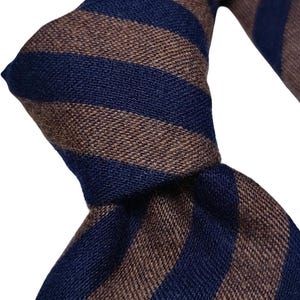 Peut inclure: Gros plan sur une cravate à rayures marron et bleu marine alternées. La cravate est nouée, mettant en valeur la texture du tissu et le contraste des couleurs. Le design est classique et adapté aux tenues formelles ou professionnelles.