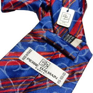 Può includere: Una cravatta di seta blu con strisce rosse e un motivo a spirale azzurro. L'etichetta recita "PIERRE BALMAIN PARIS MADE IN FRANCE". La cravatta è in 100% seta.
