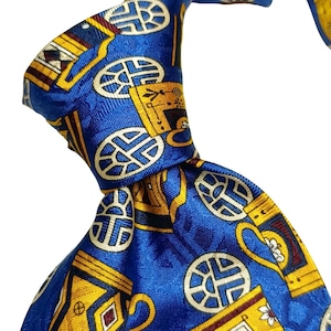 Può includere: Una cravatta di seta blu con un motivo ripetuto di elementi decorativi gialli e bianchi. La cravatta è annodata, mostrando l'intricato design e i colori vivaci. Il motivo include tazze stilizzate e forme circolari.
