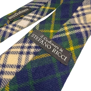 May include: A blue, green, and yellow plaid tie made of 100% cashmere. The tie features a label that reads "il Cashmere di STEFANO RICCI". The tie is knotted and displayed against a white background.