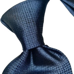 Könnte beinhalten: Eine marineblaue Krawatte mit einem dezenten Gittermuster. Die Krawatte ist geknotet und zeigt die Textur und den Glanz des Stoffes. Die Nahaufnahme zeigt die Details des gewebten Designs, geeignet für formelle oder geschäftliche Anlässe.