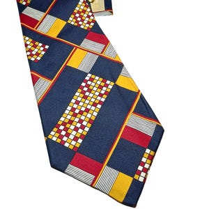 Peut inclure: Une cravate bleu marine avec un motif géométrique de carrés et de rayures rouges, jaunes, blancs et noirs. La cravate est nouée en haut et porte une étiquette dorée.