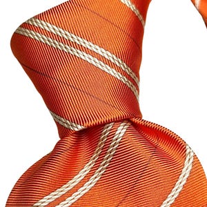 May include: Close-up of a knotted orange tie with white and silver stripes. The tie is made of a ribbed fabric, and the stripes run diagonally across the tie. The tie is a classic accessory.