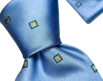May include: A light blue silk tie with a repeating pattern of small squares. Each square has a green border and a gold center. The tie is knotted and displayed against a white background.