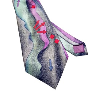 Può includere: Cravatta colorata con un design astratto unico. La cravatta presenta un motivo di linee ondulate nelle tonalità del blu, viola e verde, accentuato da frecce e quadrati rossi. La cravatta è annodata in alto.