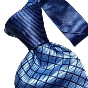 Pode incluir: Uma gravata azul com um padrão geométrico. A gravata está atada, mostrando uma combinação de seções sólidas e estampadas. O corpo principal apresenta um design de grade azul claro, enquanto o nó e a outra extremidade são de um azul escuro sólido.