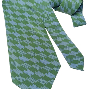 May include: Green and blue patterned tie with a repeating geometric design. The tie features a light blue and green color scheme. The tie has a logo near the knot. The tie is made of a smooth fabric.