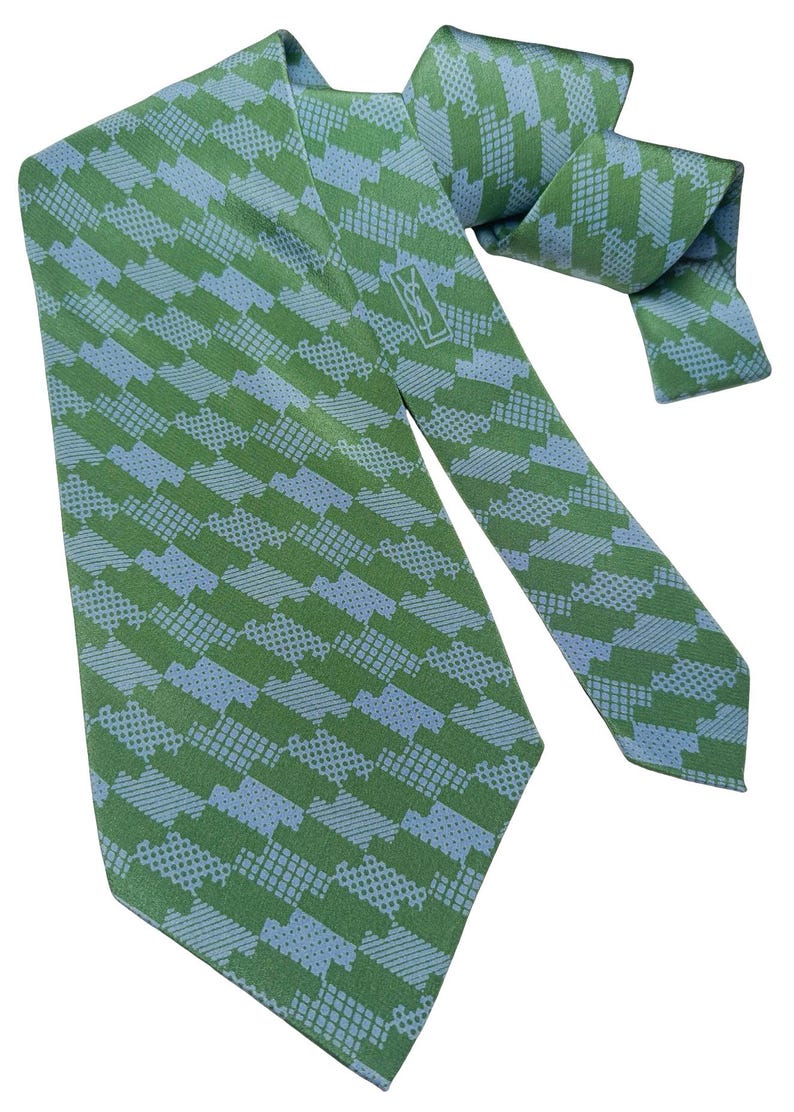 May include: Green and blue patterned tie with a repeating geometric design. The tie features a light blue and green color scheme. The tie has a logo near the knot. The tie is made of a smooth fabric.