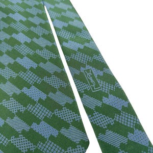 May include: Green and blue patterned tie. The tie features a repeating geometric design in shades of green and blue. The YSL logo is visible near the tip of the tie. The tie is made of a smooth fabric.