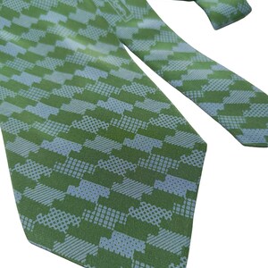May include: Green and light blue patterned necktie. The tie features a repeating geometric design in shades of green and light blue. The tie is made of a smooth fabric and is suitable for formal or business attire.