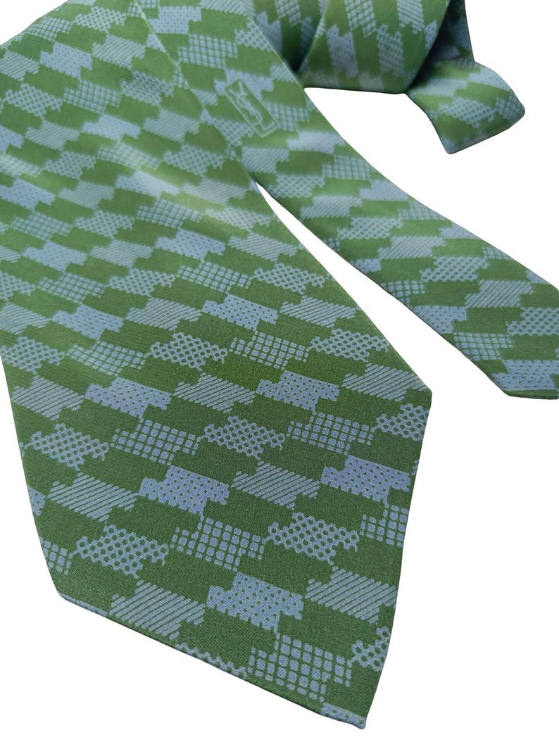 May include: Green and light blue patterned necktie. The tie features a repeating geometric design in shades of green and light blue. The tie is made of a smooth fabric and is suitable for formal or business attire.