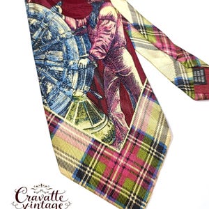 May include: Vintage silk tie featuring a nautical illustration of a man at a ship's wheel in shades of blue, red, and cream. The tie has a plaid pattern in pink, green, and yellow. The brand name "Cravatte vintage" is printed on the tie.