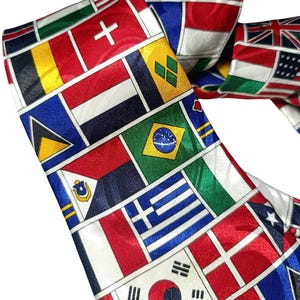 May include: A patterned silk tie displaying a collage of international flags. The flags are in various rectangular shapes and feature colours like red, white, blue, and green. The tie is folded, revealing both sides of the fabric.