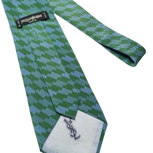 May include: Green and blue patterned silk tie. The tie features a repeating geometric design in shades of green and blue. The label reads "Yves Saint Laurent Paris". The tie is made of silk.