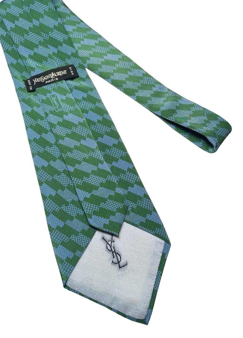 May include: Green and blue patterned silk tie. The tie features a repeating geometric design in shades of green and blue. The label reads "Yves Saint Laurent Paris". The tie is made of silk.