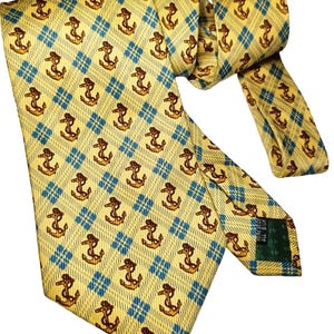 May include: Yellow tie with a repeating pattern of brown anchors within blue diamond shapes. The tie is made of a shiny material and is knotted. The tie is a classic accessory for formal or business attire.