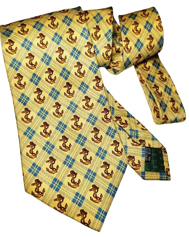 May include: Yellow tie with a repeating pattern of brown anchors within blue diamond shapes. The tie is made of a shiny material and is knotted. The tie is a classic accessory for formal or business attire.