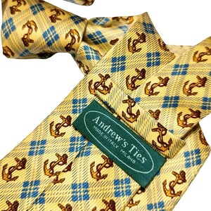 May include: A yellow tie with a repeating pattern of brown anchors and blue diamond shapes. The tie has a label that reads "Andrew's Ties MADE IN ITALY MILANO".