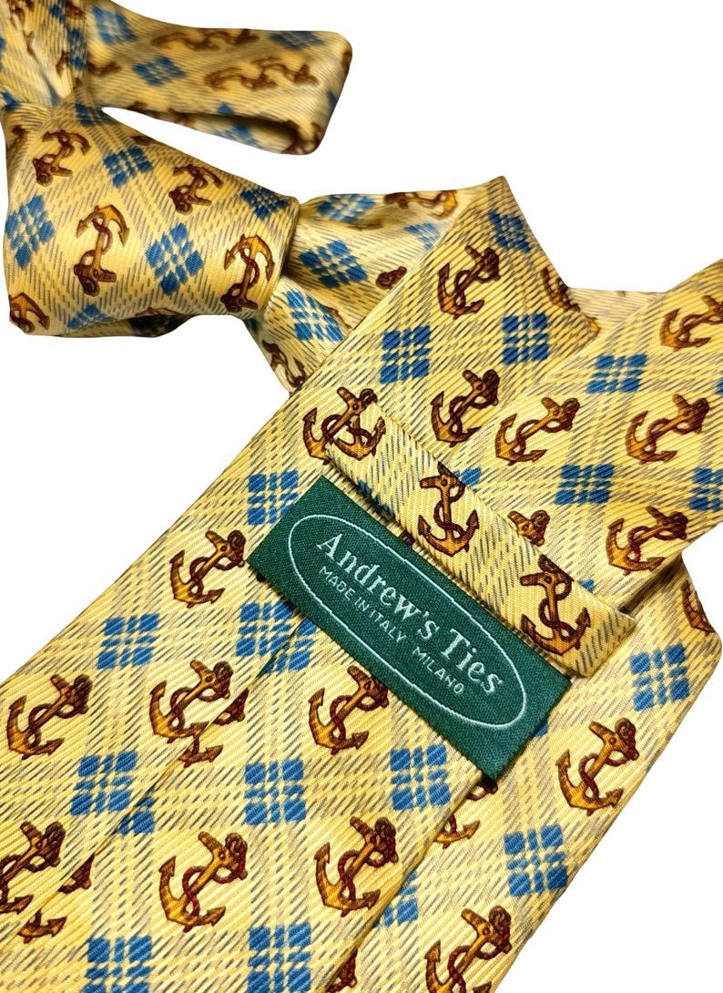 May include: A yellow tie with a repeating pattern of brown anchors and blue diamond shapes. The tie has a label that reads "Andrew's Ties MADE IN ITALY MILANO".