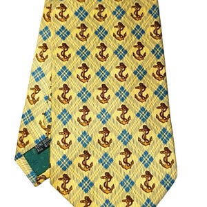 May include: Yellow silk tie with a repeating pattern of brown anchors set within blue diamond shapes. The tie is folded, showing the pattern and the label "FINE SEID ALL SILK".