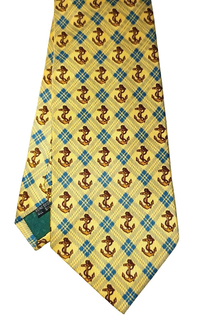 May include: Yellow silk tie with a repeating pattern of brown anchors set within blue diamond shapes. The tie is folded, showing the pattern and the label "FINE SEID ALL SILK".