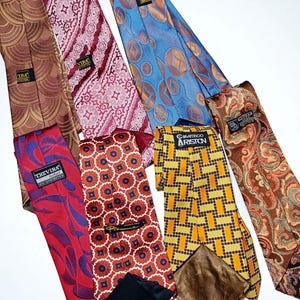 Puede incluir: Una colección de corbatas estampadas en varios colores, incluyendo marrón, burdeos, azul y naranja. Las corbatas presentan diseños geométricos, florales y de cachemira. Algunas corbatas tienen etiquetas con texto.
