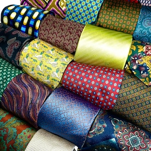 Può includere: Una collezione di cravatte arrotolate in vari colori e fantasie. Le cravatte presentano una gamma di design, tra cui paisley, forme geometriche, floreali e stampe fantasiose. I colori includono blu, rosso, verde, giallo e marrone.