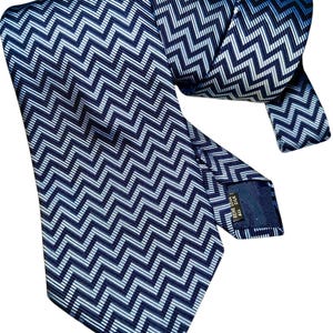 May include: A navy blue tie featuring a repeating white and light blue zigzag pattern. The tie is made of a shiny material and is folded over itself. The tie has a label on the back.