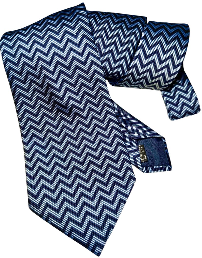 May include: A navy blue tie featuring a repeating white and light blue zigzag pattern. The tie is made of a shiny material and is folded over itself. The tie has a label on the back.
