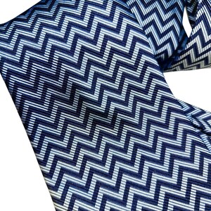 May include: A close-up of a blue and white patterned tie. The tie has a repeating zigzag design in shades of blue and white. The fabric appears smooth and the pattern is consistent across the tie.