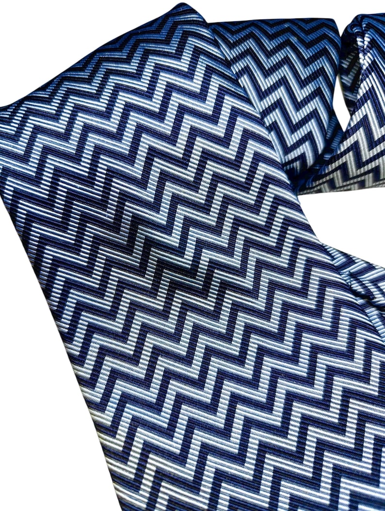 May include: A close-up of a blue and white patterned tie. The tie has a repeating zigzag design in shades of blue and white. The fabric appears smooth and the pattern is consistent across the tie.