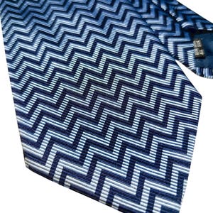 May include: A blue and white zigzag patterned tie. The tie displays a repeating chevron design in shades of blue and white. The fabric has a subtle sheen, and the tie is angled, showcasing the pattern's direction.